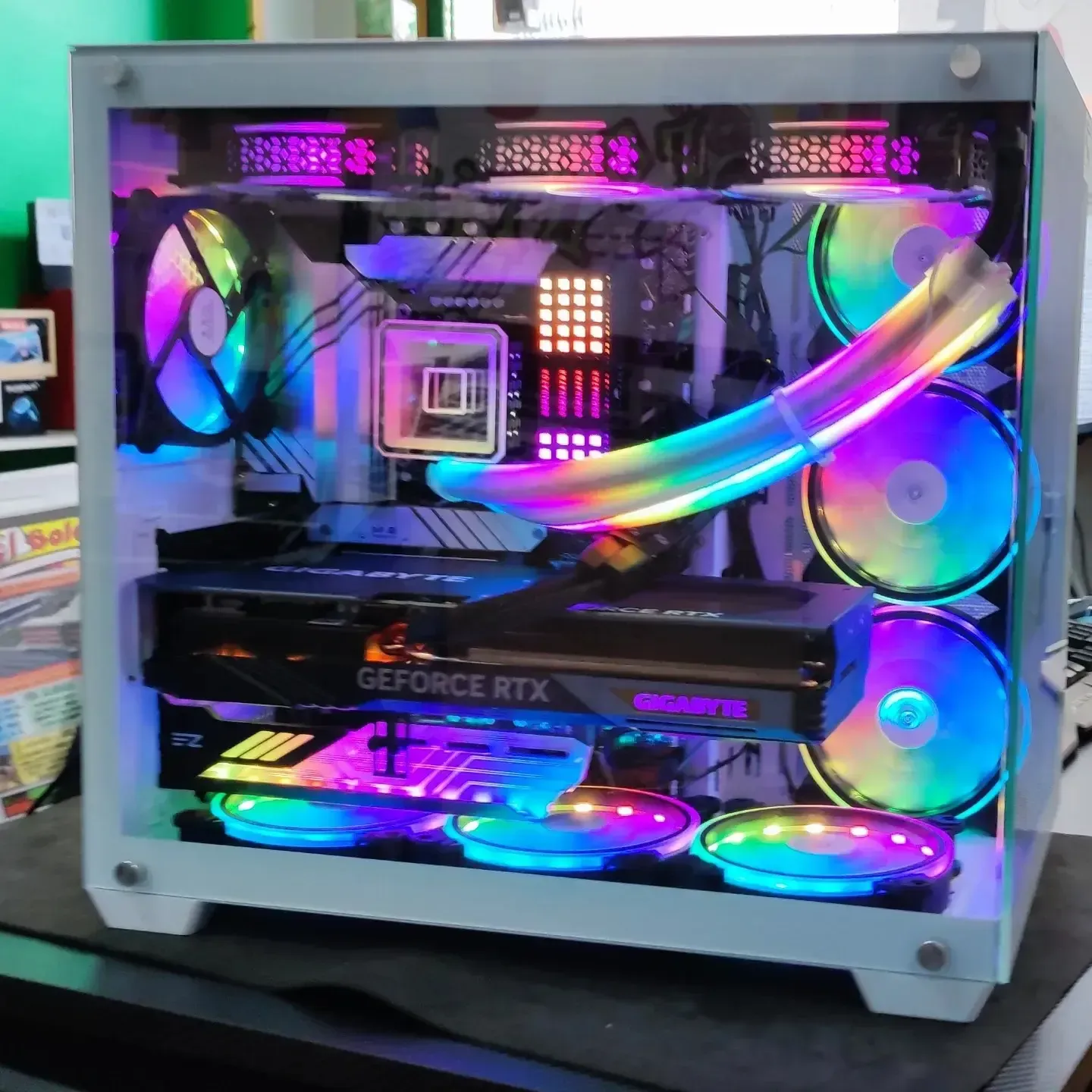 PC para juegos con iluminación RGB dentro de una carcasa blanca, que muestra ventiladores arcoíris y componentes iluminados a través de un panel lateral transparente.