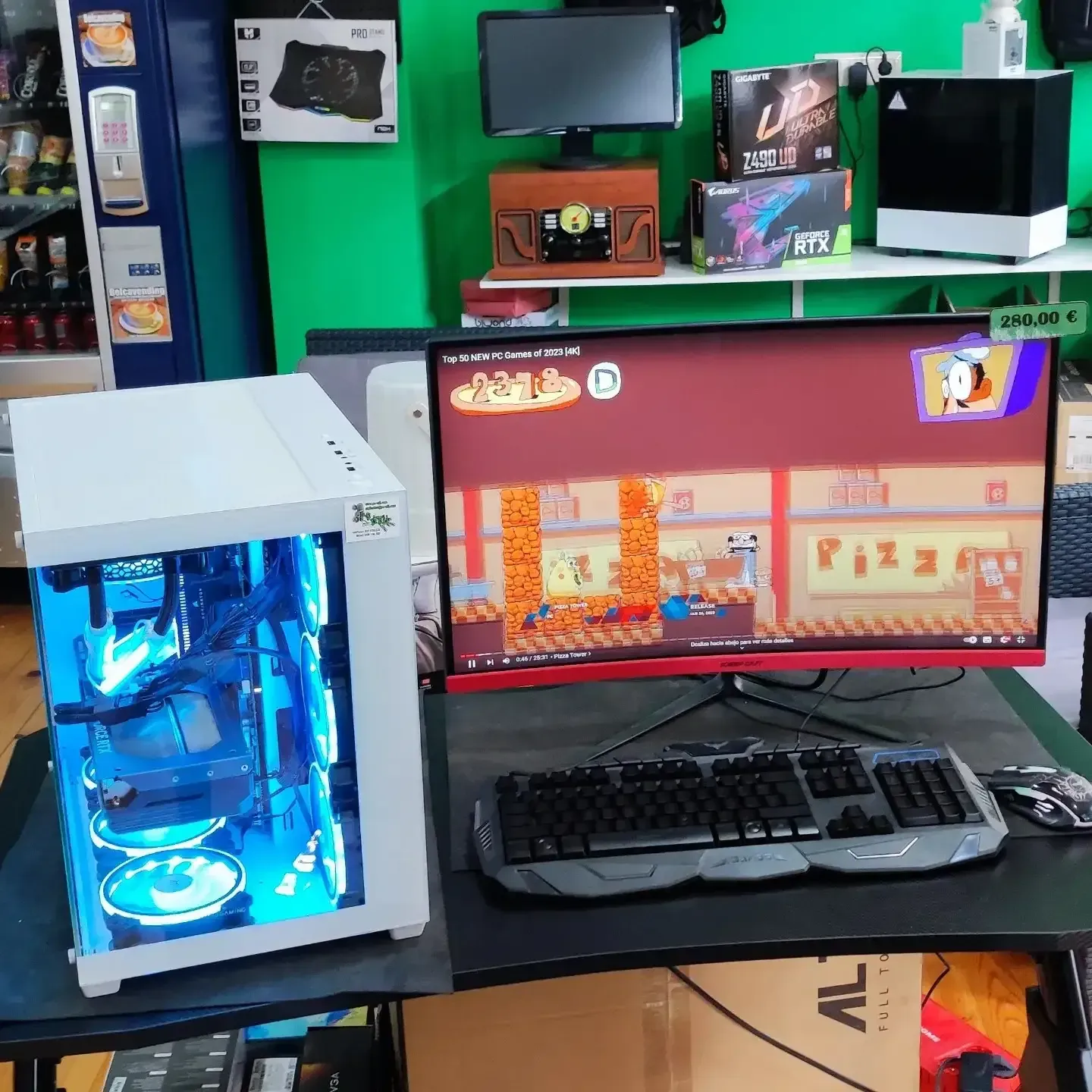 Escritorio para videojuegos con una torre de PC blanca que emite una luz azul junto a un monitor que muestra una escena de juego.