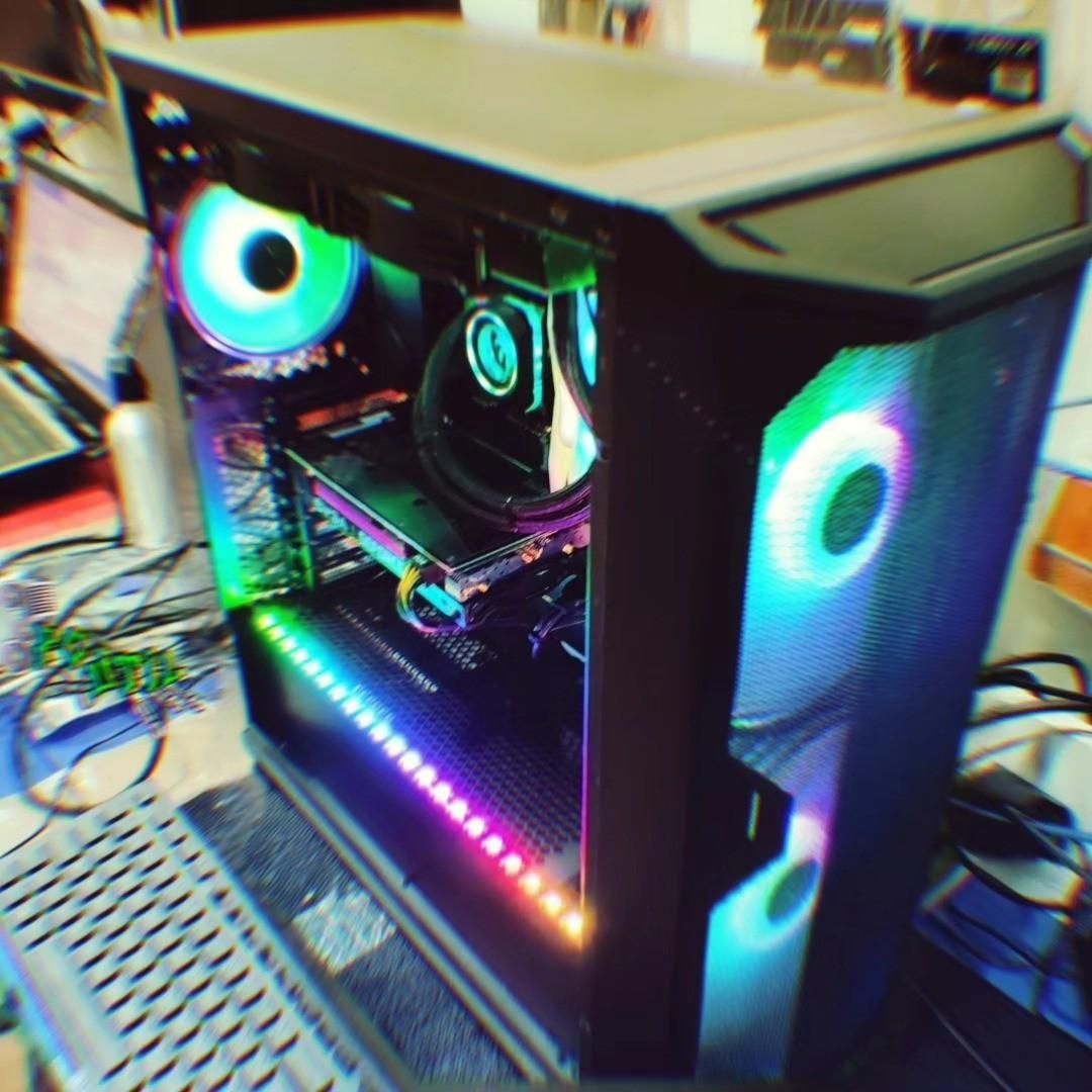 Torre de PC para juegos con iluminación RGB, panel lateral de cristal, ventiladores luminosos y teclado sobre un escritorio.