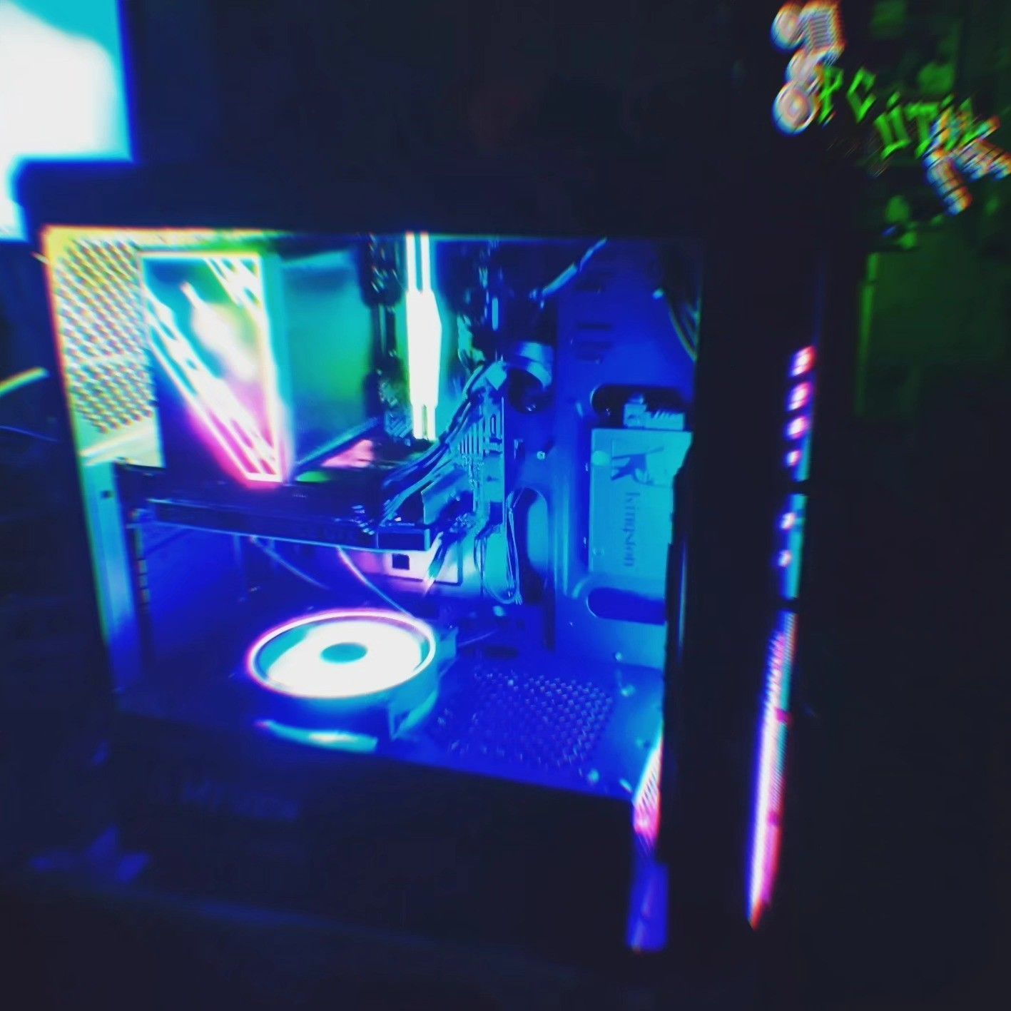 Torre de PC para juegos con iluminación RGB, ventilador brillante y componentes internos coloridos en una habitación oscura.
