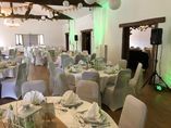 Une salle de banquet aménagée pour une réception de mariage avec des tables rondes, du linge blanc et des housses de chaise.