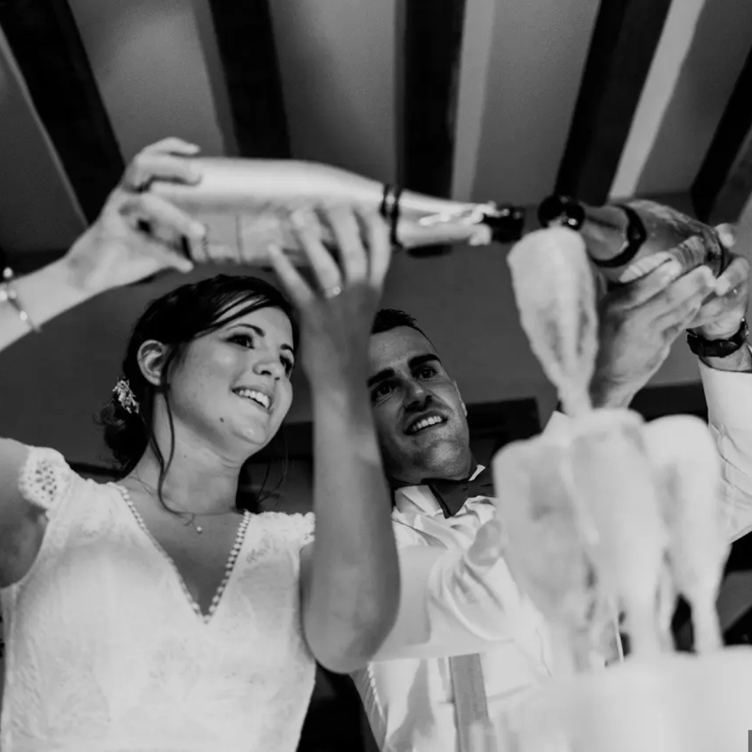 Un couple verse du champagne dans des flûtes lors d'une célébration de mariage, avec le sourire.
