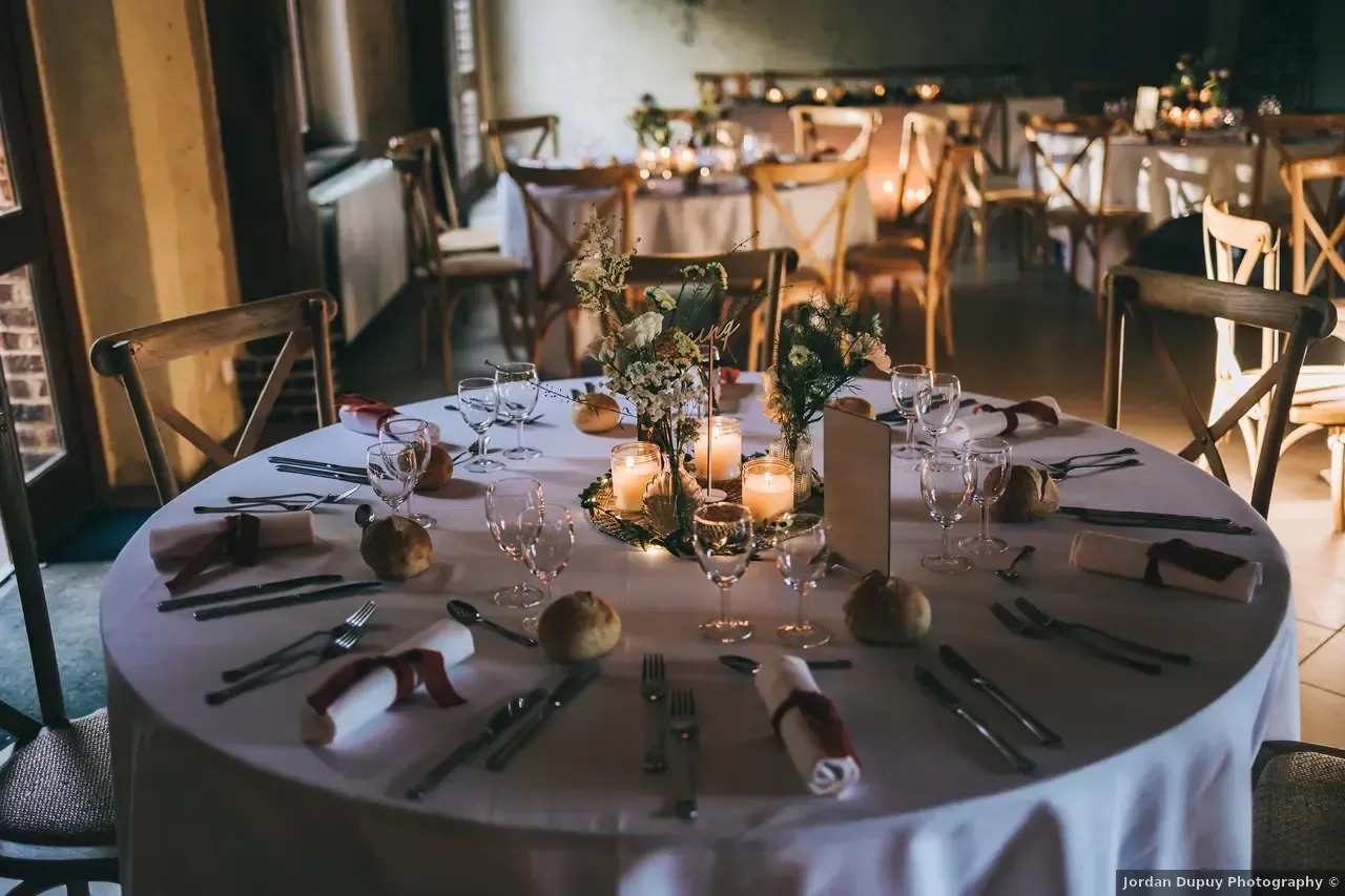 Tables rondes dressées pour une réception de mariage avec centres de table et bougies.