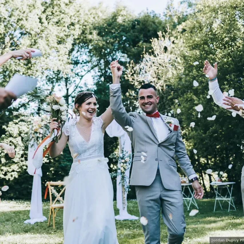 Les mariés lèvent les bras, couverts de confettis, lors d'une cérémonie de mariage en plein air.