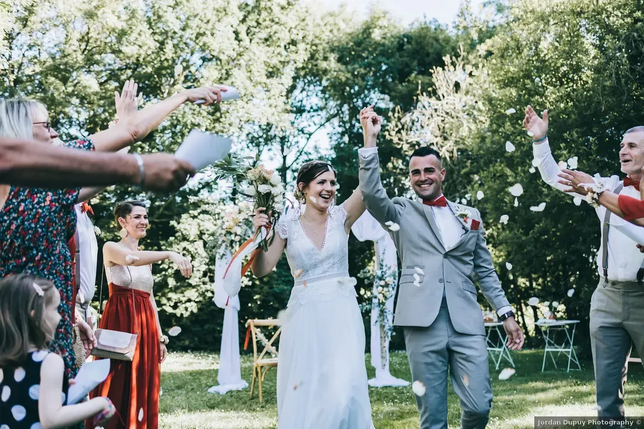 Les jeunes mariés lèvent les mains au milieu des confettis, célébrant leur mariage dans un jardin.