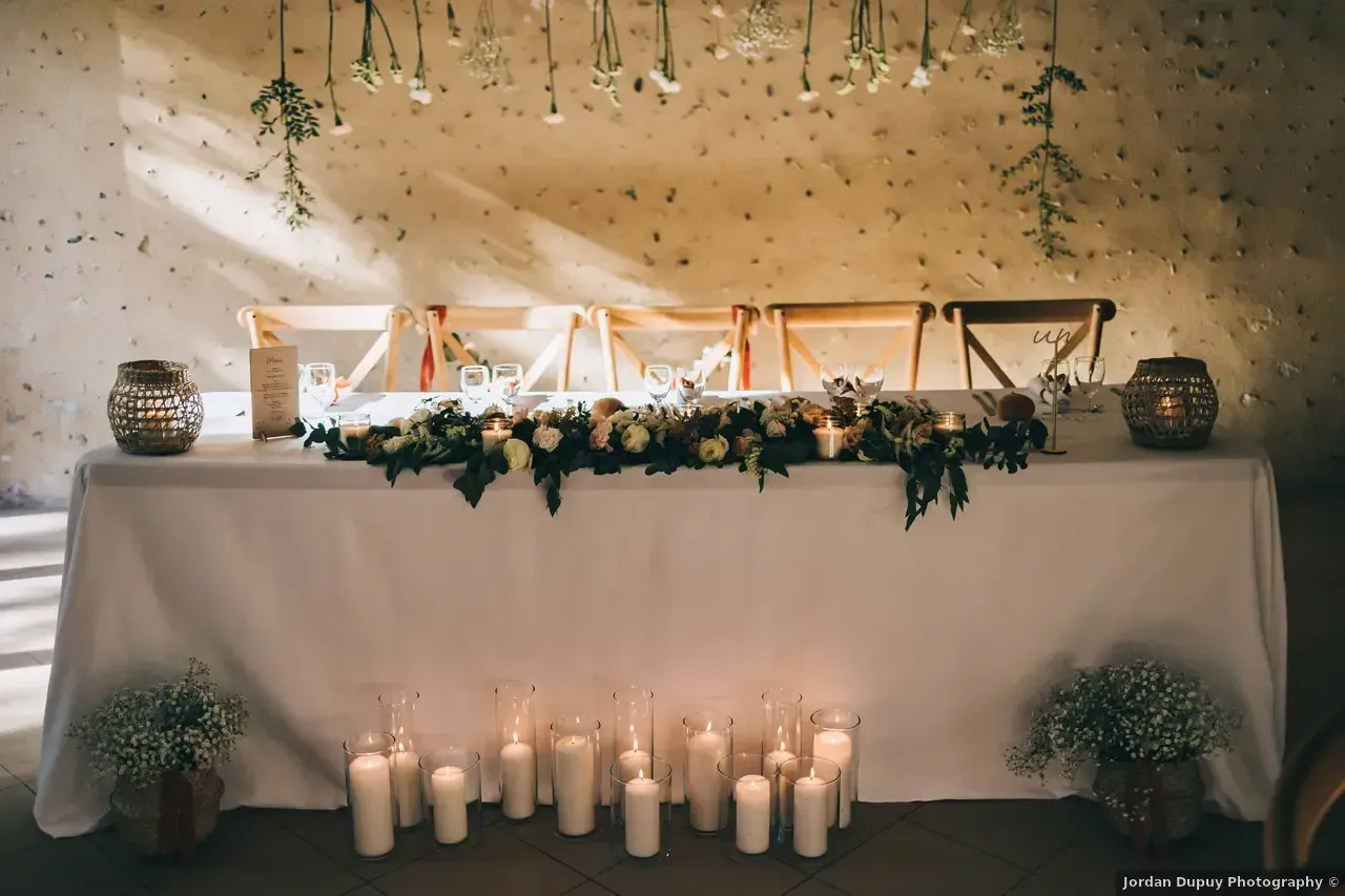 Ensemble de table de réception de mariage avec nappe blanche, guirlande florale, bougies et fleurs suspendues.