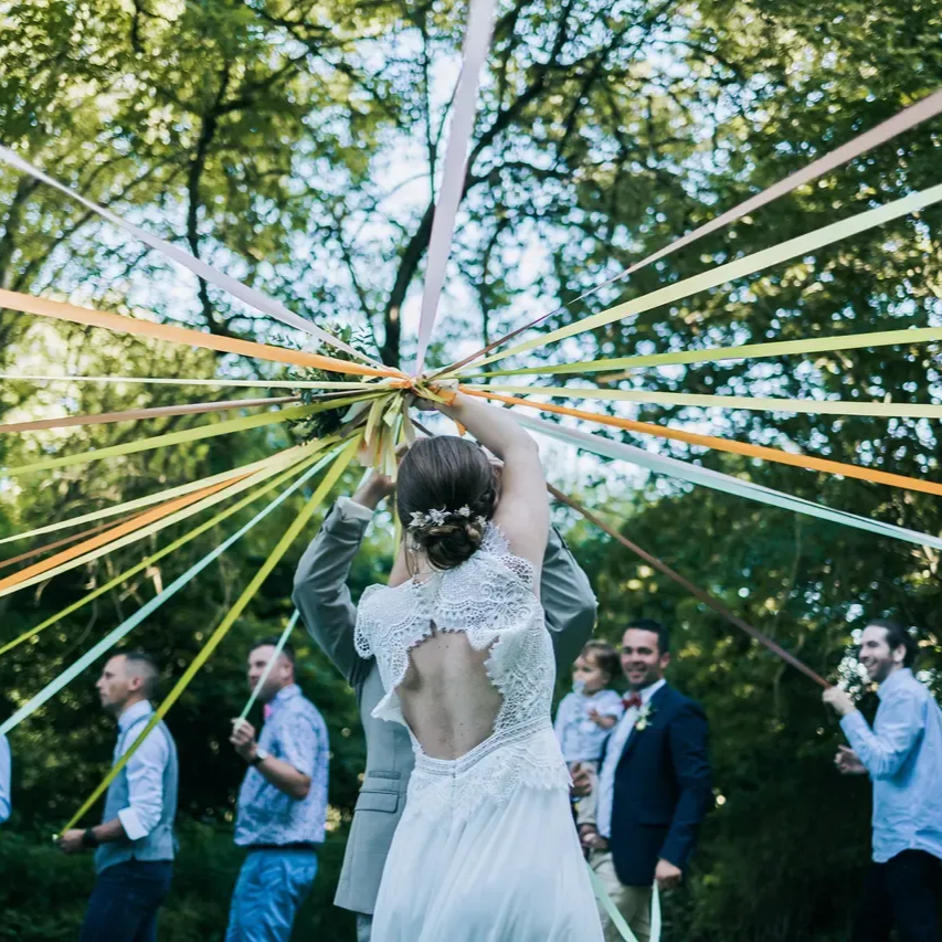 Couple de mariés tenant des rubans lors d'une cérémonie en plein air. Les invités tiennent également les extrémités.