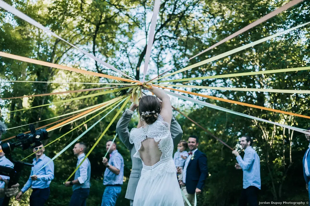 Les mariés dansent sous des rubans dans une forêt. Les invités regardent, les rubans à la main.