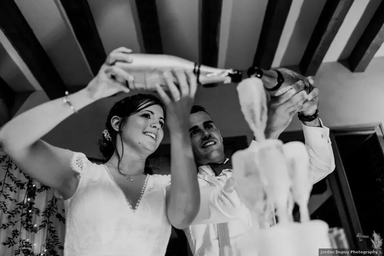 Les mariés versent du champagne dans des verres empilés sur un gâteau, expressions joyeuses.