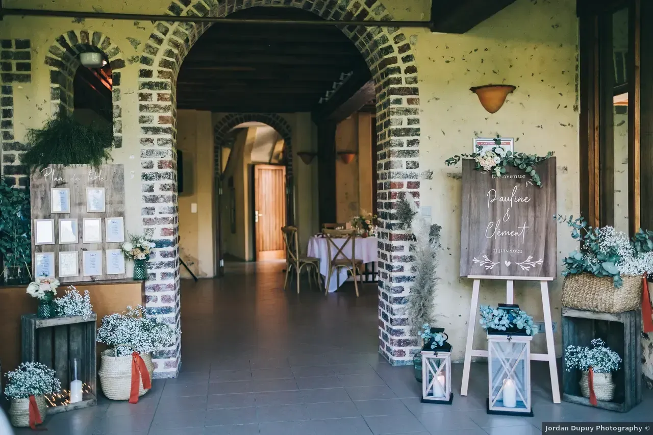 Entrée de réception de mariage avec décor rustique : arches en briques, panneaux en bois, fleurs et lanternes.