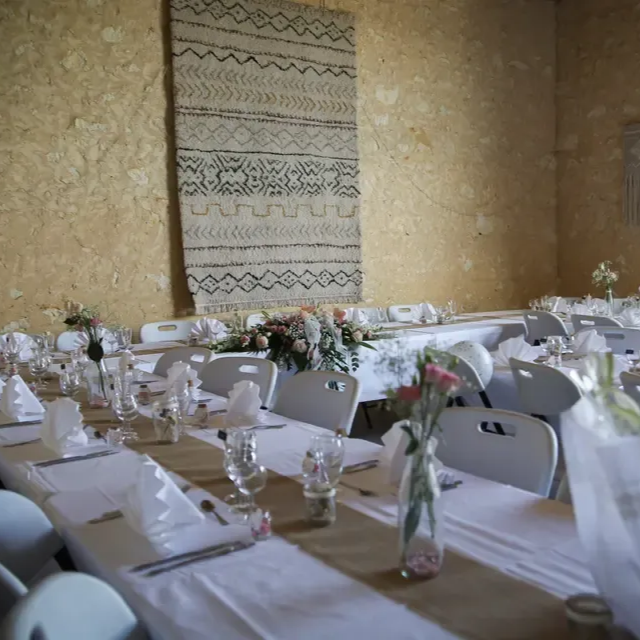 De longues tables dressées pour une réception de mariage dans une salle avec des murs en pierre.