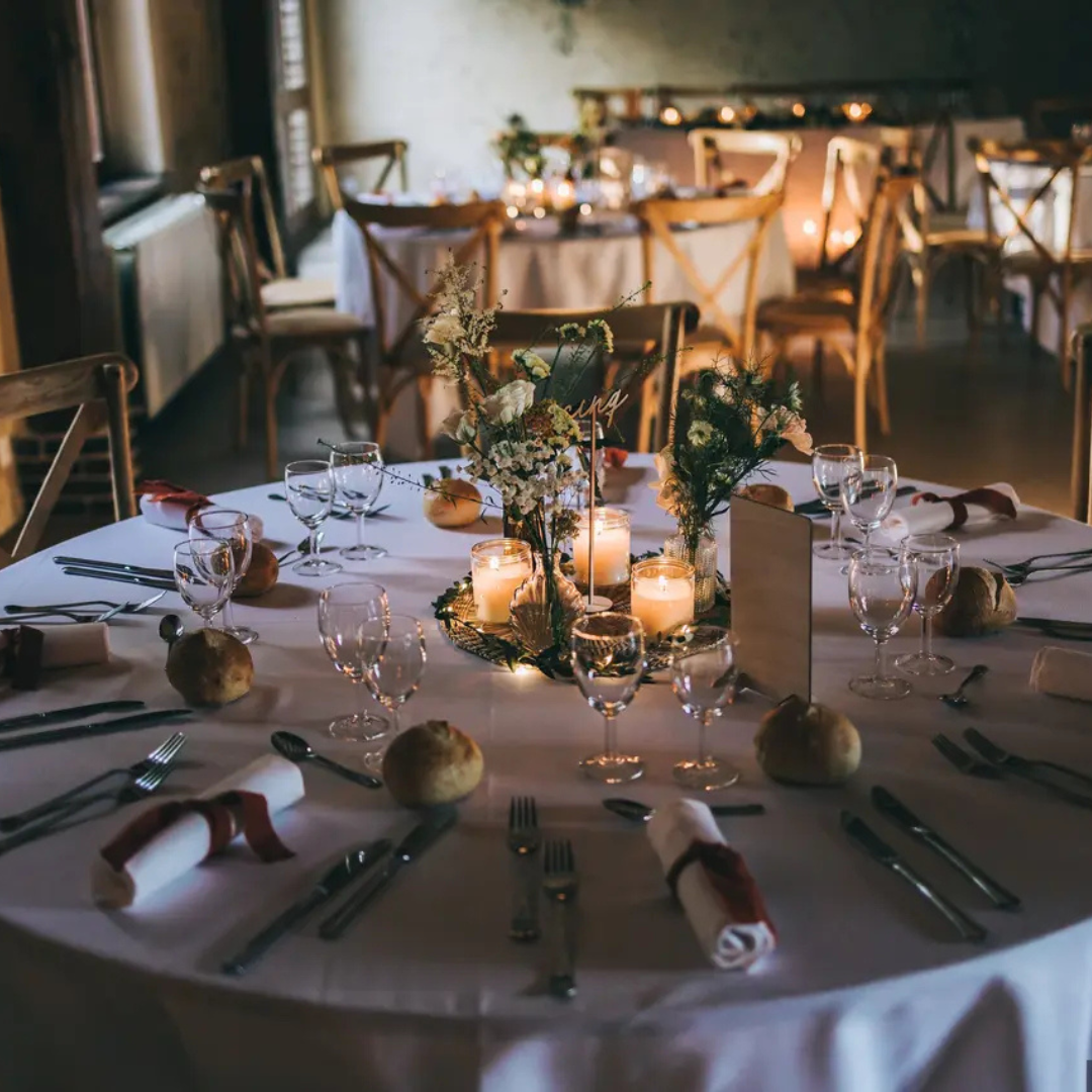 Ensemble de table ronde pour une réception de mariage avec centres de table, bougies et couverts.