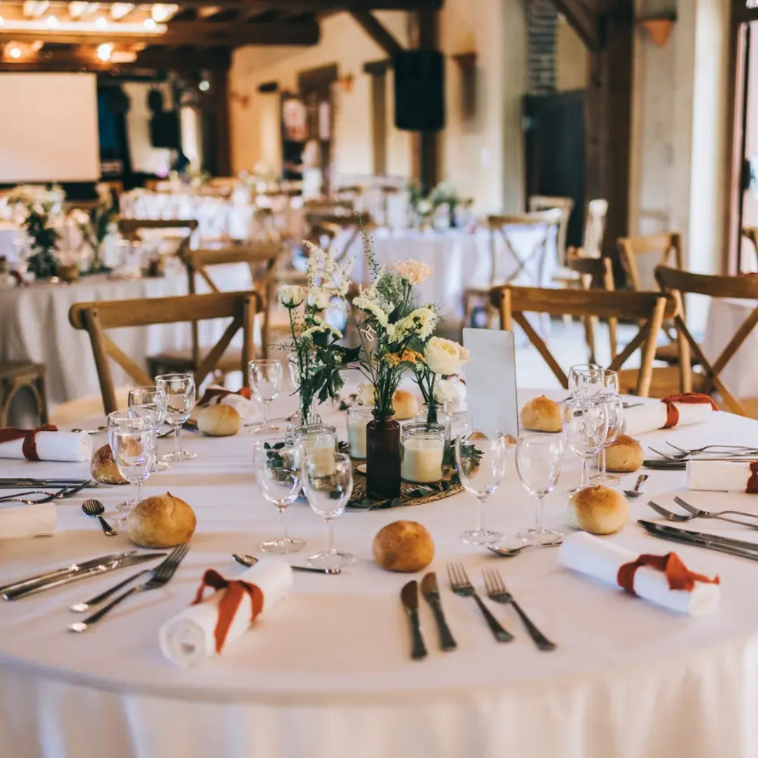 Table ronde dressée pour un événement formel, comprenant des compositions florales.