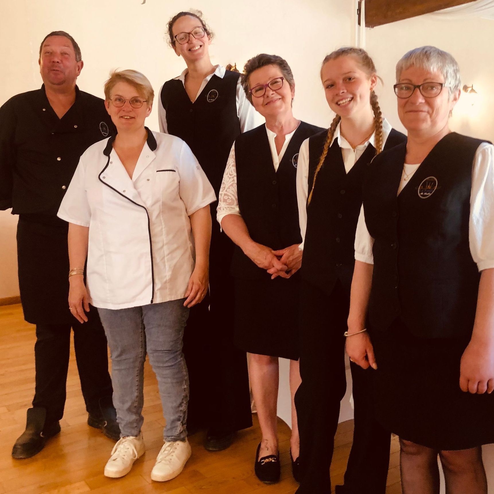 Le personnel du restaurant pose ensemble devant un parquet clair. Certains portent des gilets noirs et des chemises blanches.