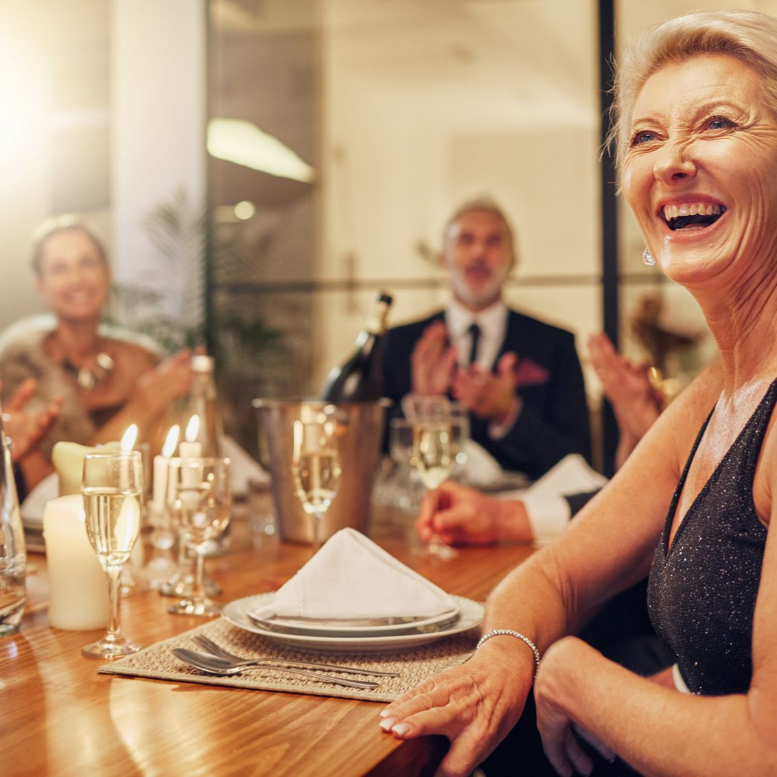 Femme riant lors d'un dîner ; bougies, champagne, tenue de soirée.