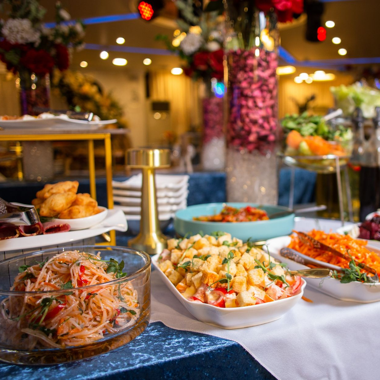 Buffet avec salades et plats variés, fleurs en arrière-plan. Décoration de table bleue et blanche.