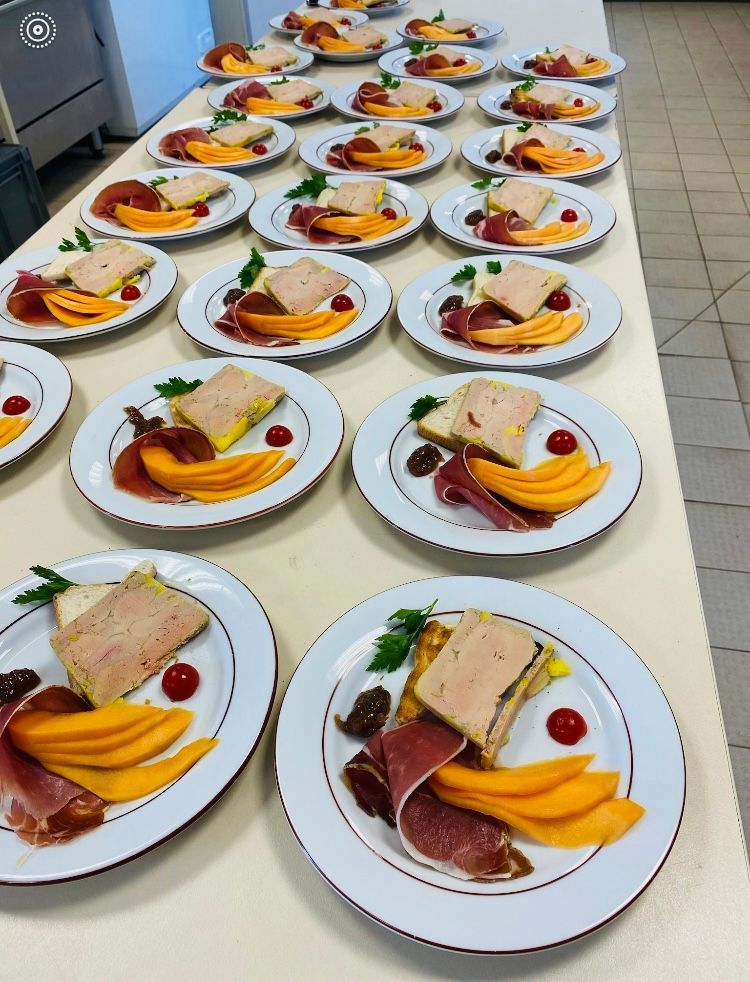 Assiettes d'entrées : foie gras, tranches de cantaloup, prosciutto et garnitures, disposées sur une longue table.
