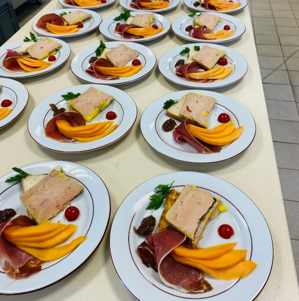 Des assiettes de nourriture, comprenant du melon, du jambon et un carré de pâté, sont disposées sur une surface blanche.