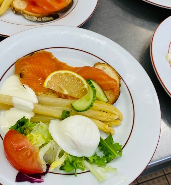 Assiette de nourriture : saumon fumé sur pain grillé, asperges, œuf, citron, tomate et légumes verts.