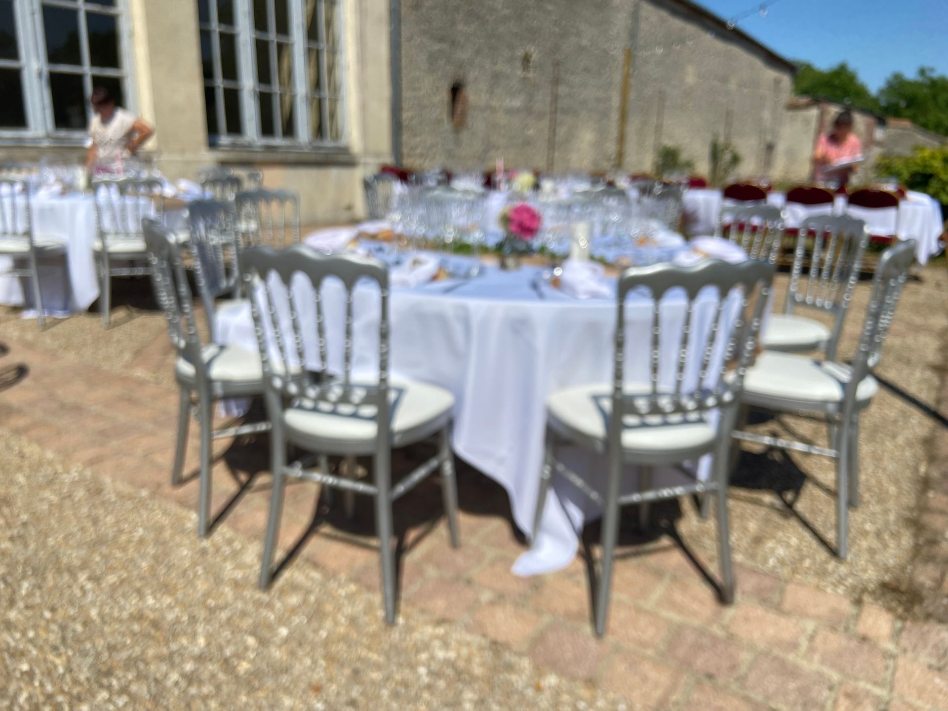 Tables de jardin dressées pour une fête. Des chaises argentées entourent des nappes blanches.