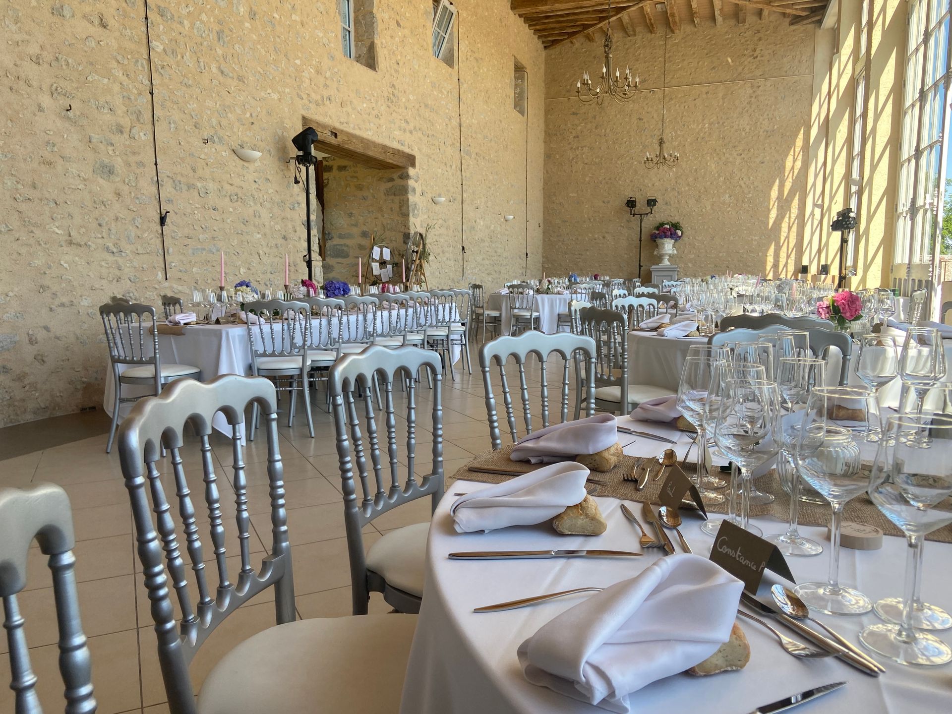 Réception de mariage aménagée dans une grande salle en pierre avec des tables rondes.