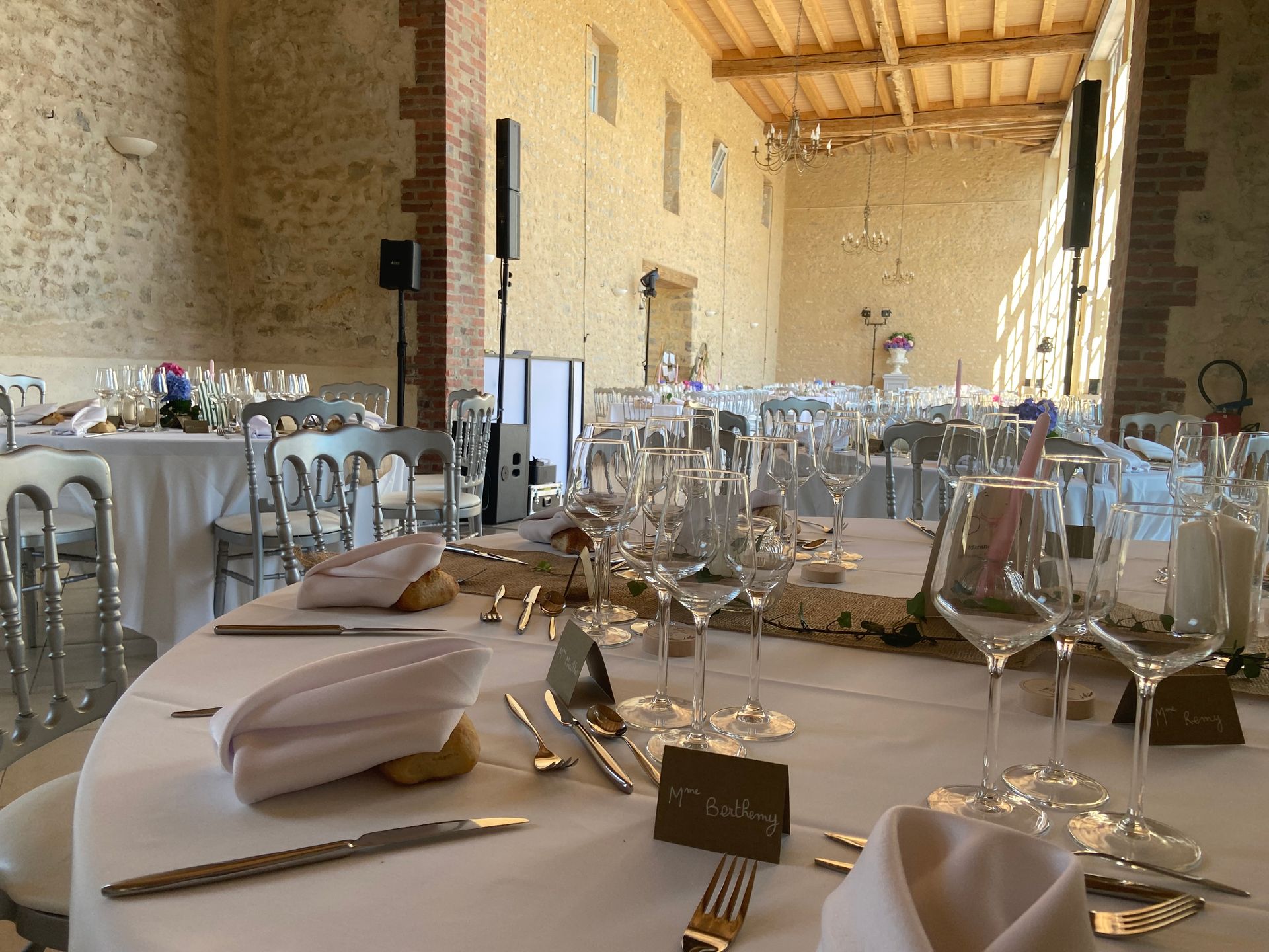 Réception de mariage aménagée dans une grande salle aux murs de pierre avec des tables rondes.