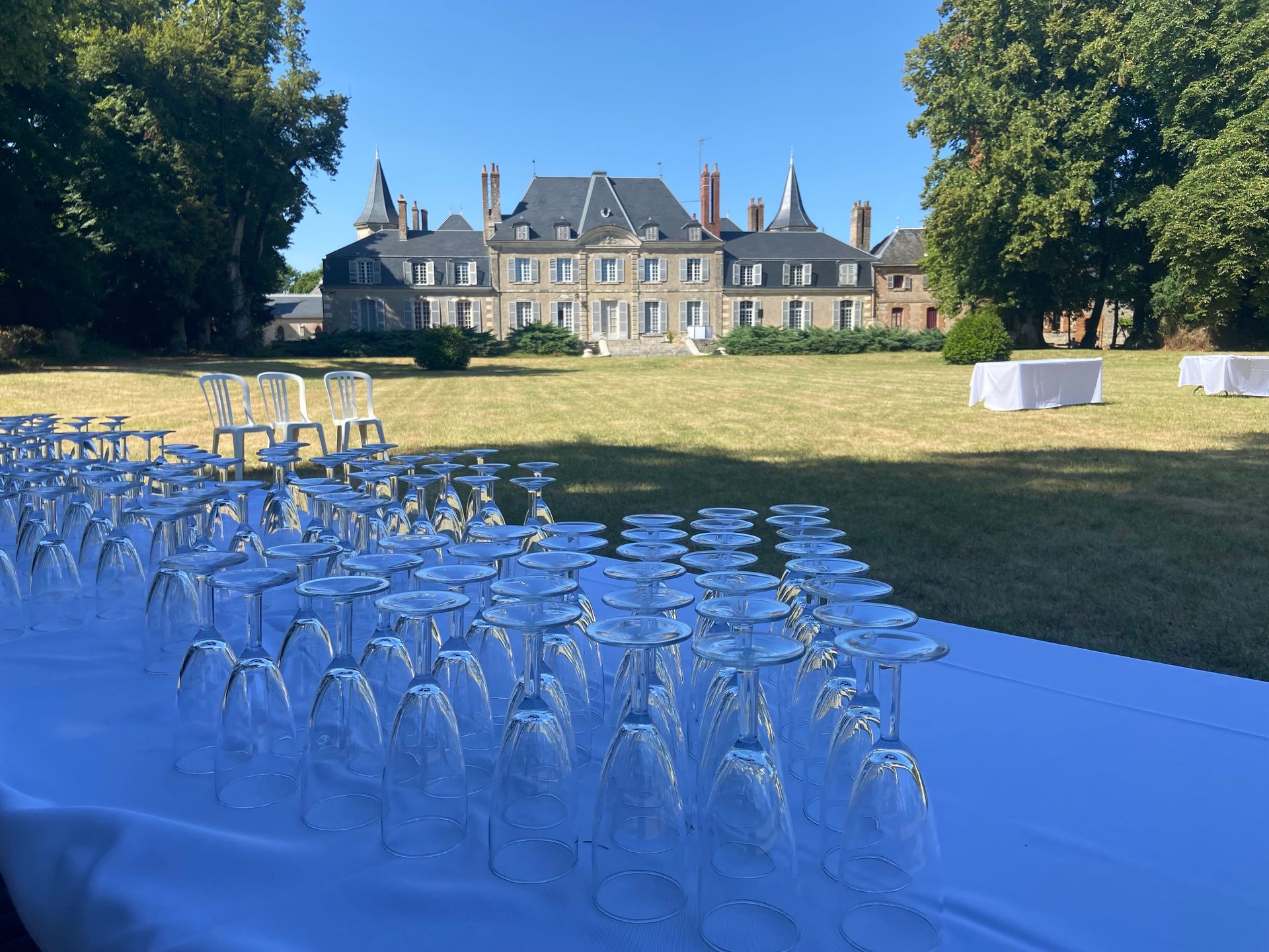 Des verres à vin disposés sur une table devant un château, installés pour un événement par une journée ensoleillée.