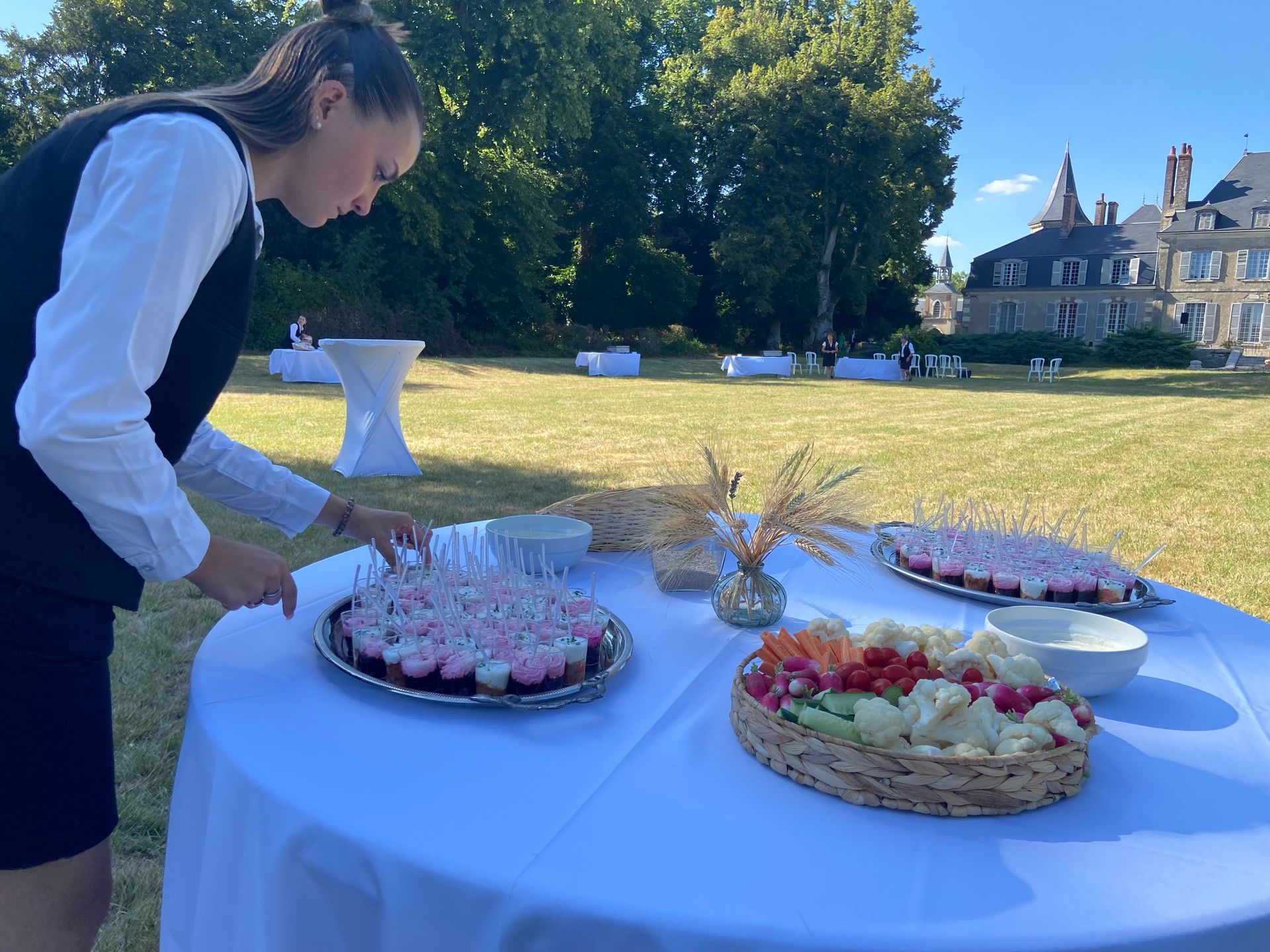Un serveur dispose des hors-d'œuvre sur une table, en préparation d'un événement en plein air devant un château.