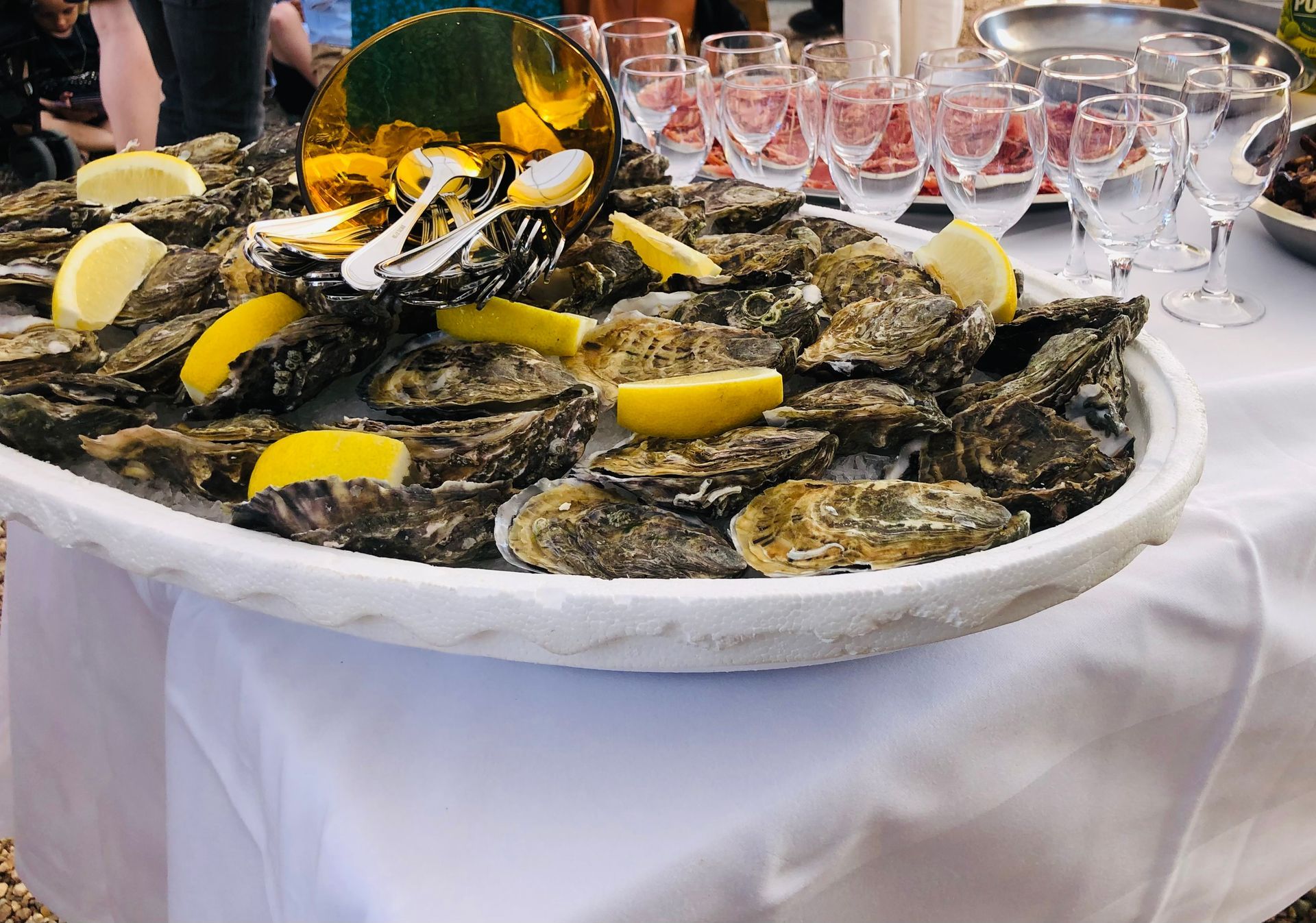 Huîtres sur un plateau avec des quartiers de citron. Des verres et un autre plat sont posés sur une nappe blanche.