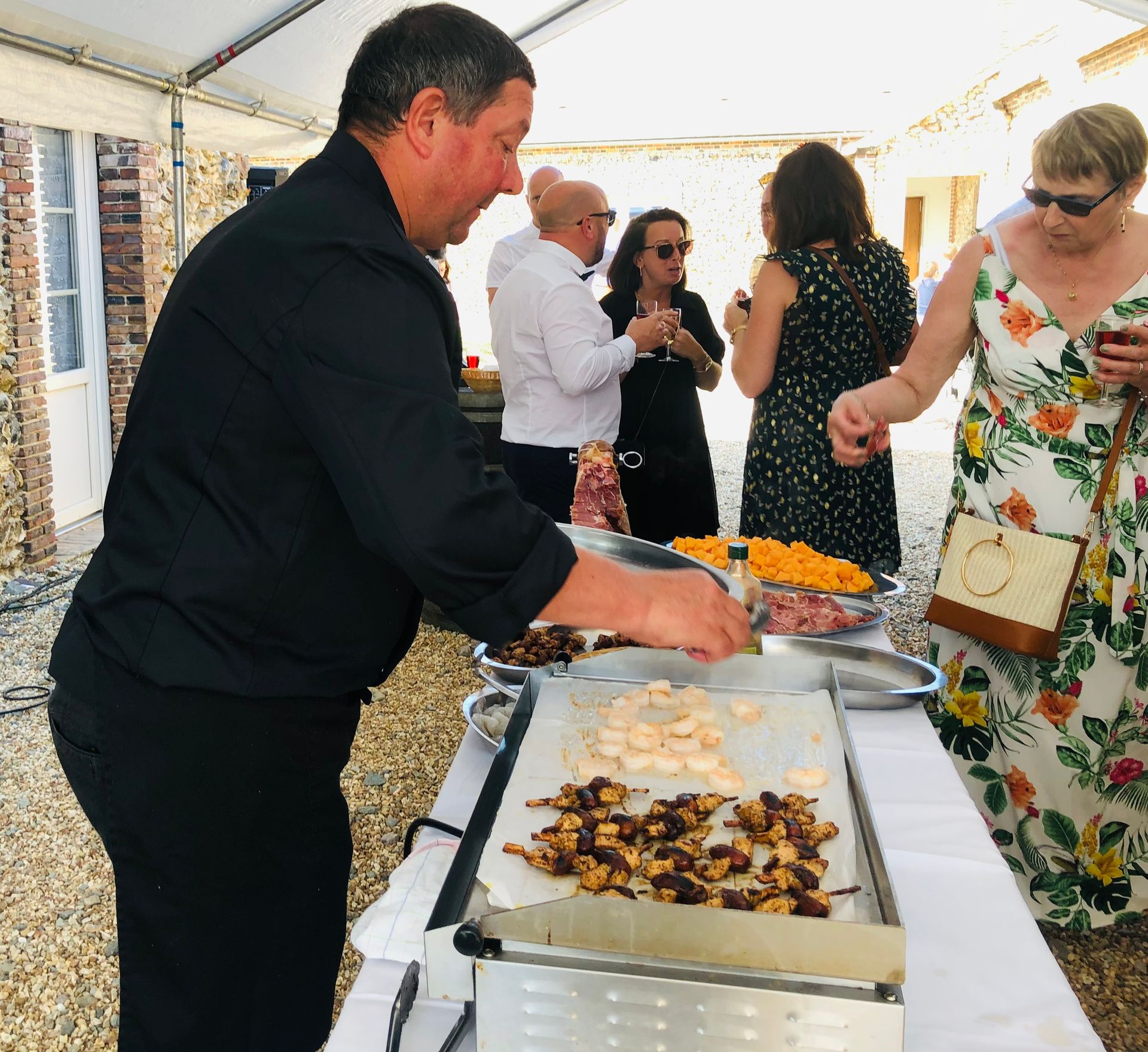 Un homme fait cuire de la nourriture sur un gril lors d'un événement en plein air, tandis que les gens regardent.