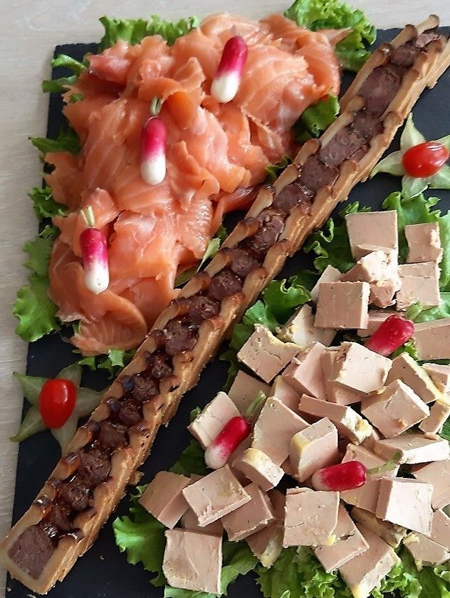 Assiette de saumon fumé, pâté et foie gras en dés avec radis et laitue sur ardoise noire.