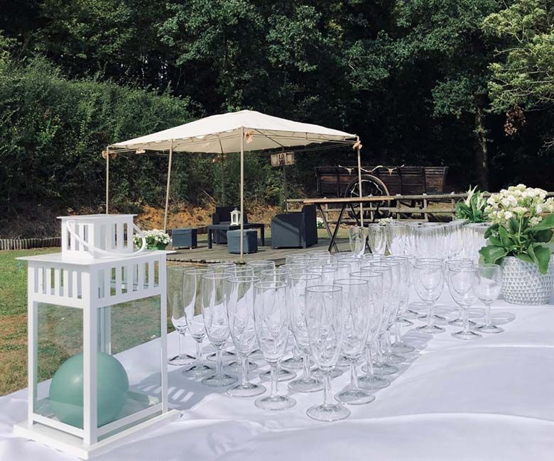 Événement en plein air avec coupes de champagne, table blanche, lanternes et tente à baldaquin dans un décor de jardin.