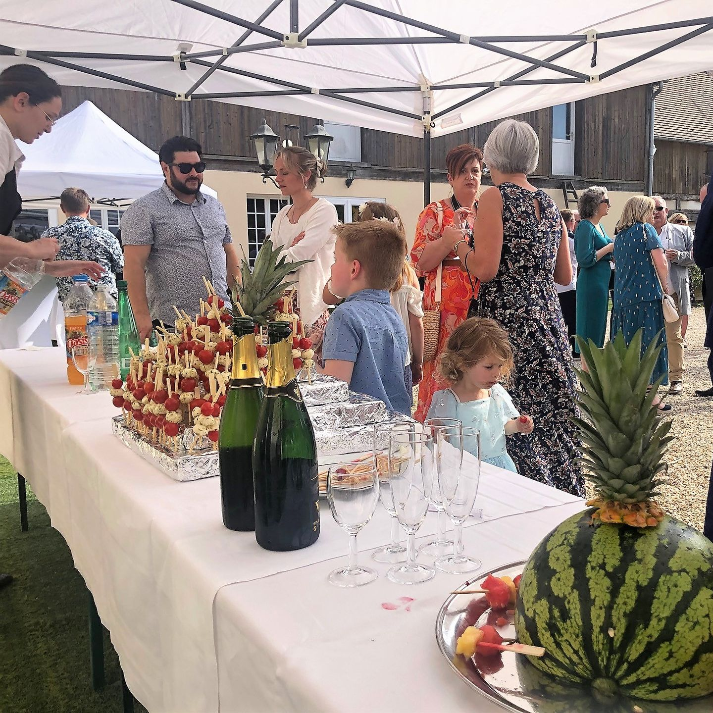 Scène de fête en plein air avec de la nourriture et des boissons sur une table recouverte de blanc.