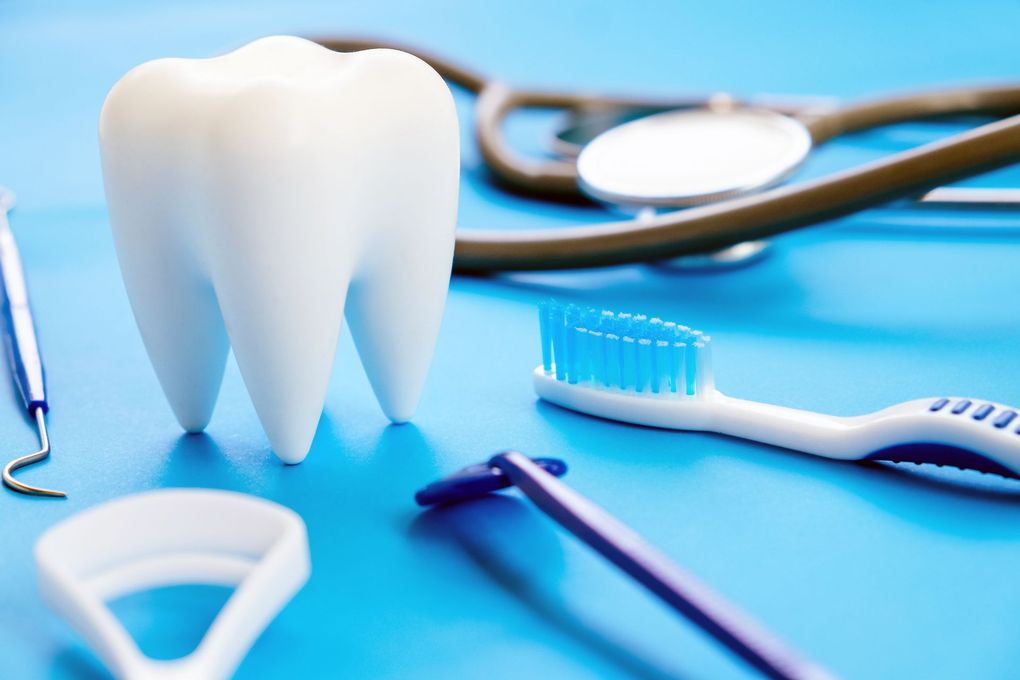Modelo de diente blanco con herramientas dentales: cepillo de dientes, estetoscopio, palillos y raspador