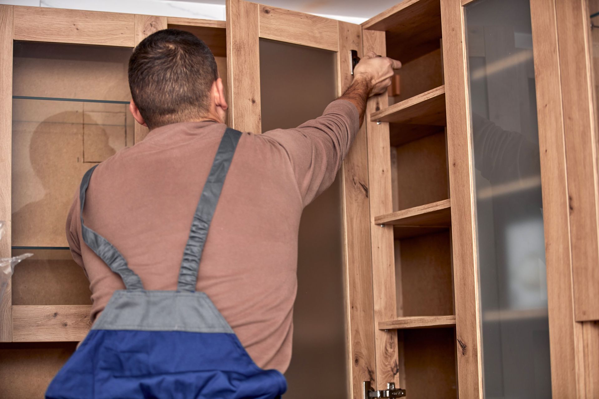 Une personne installe une structure d'armoire en bois avec des portes vitrées.