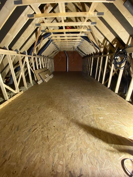Vue grand angle d'un grenier non aménagé avec des chevrons en bois.