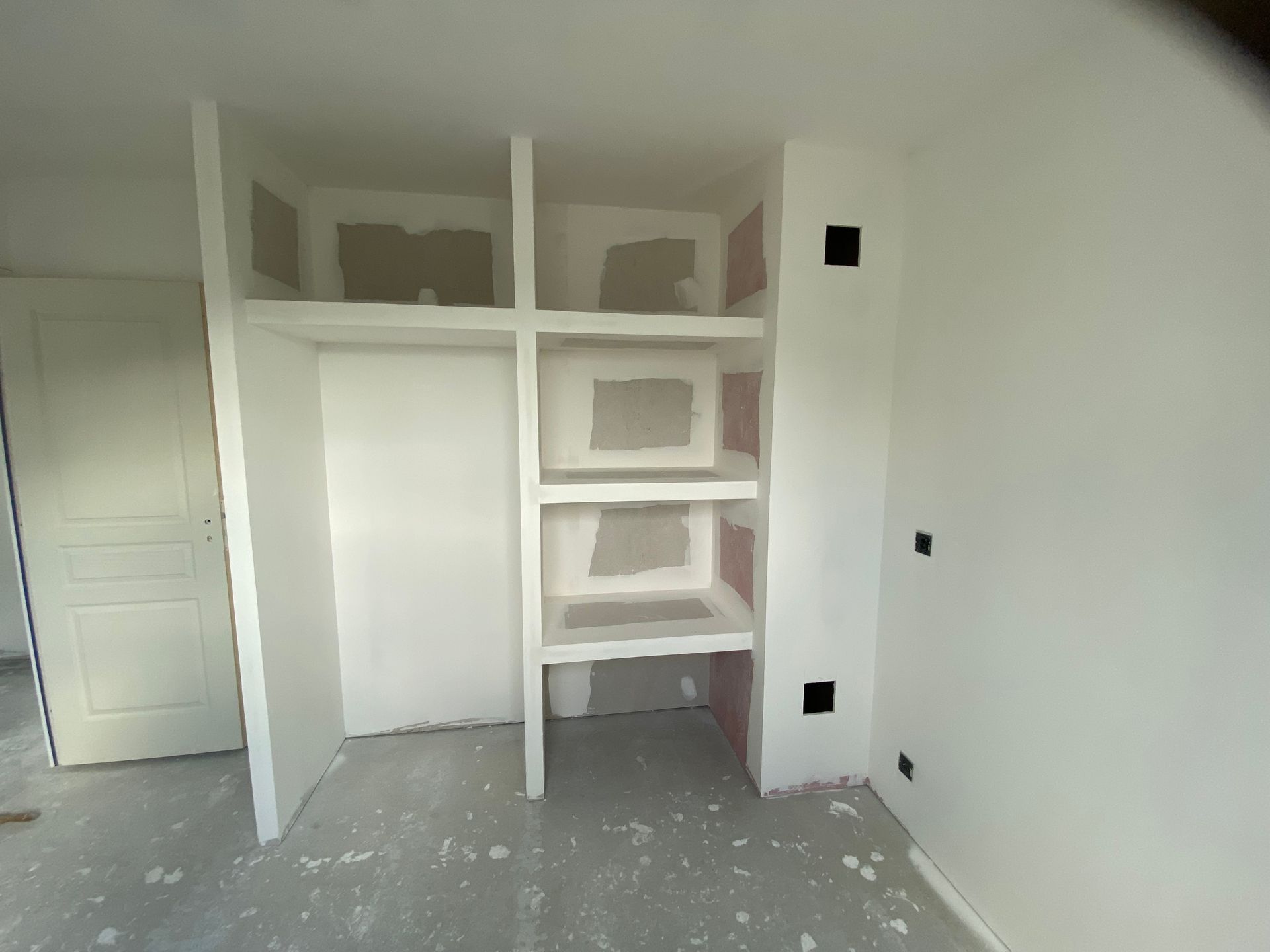 Une pièce intérieure en construction avec des cloisons sèches blanches, comprenant des étagères intégrées.