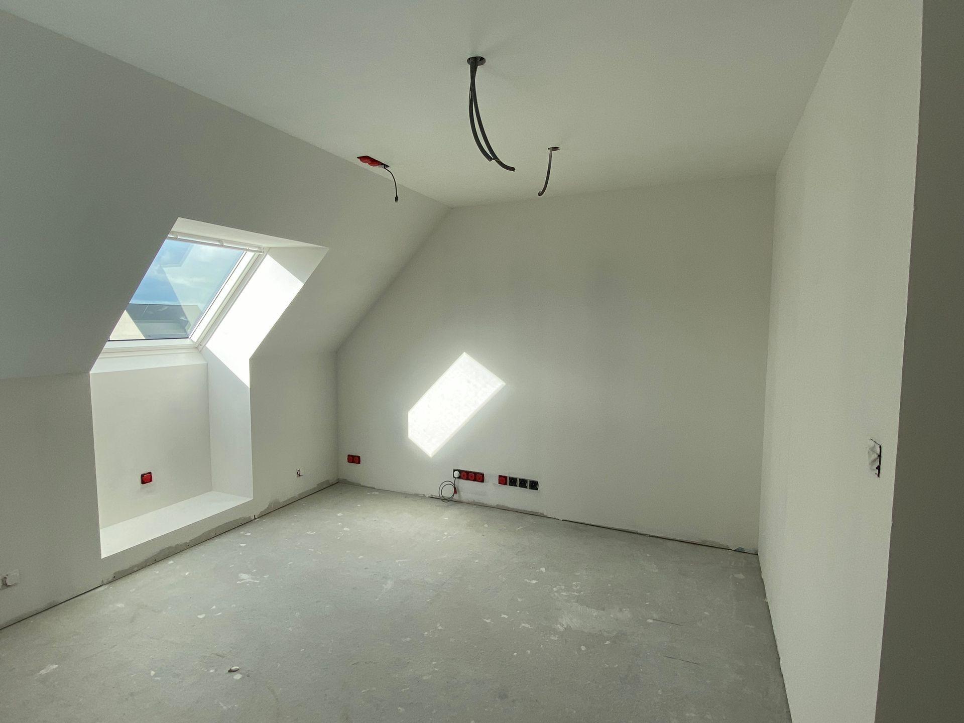 Combles non aménagés avec poutres apparentes, isolation entre les solives et une fenêtre lumineuse.