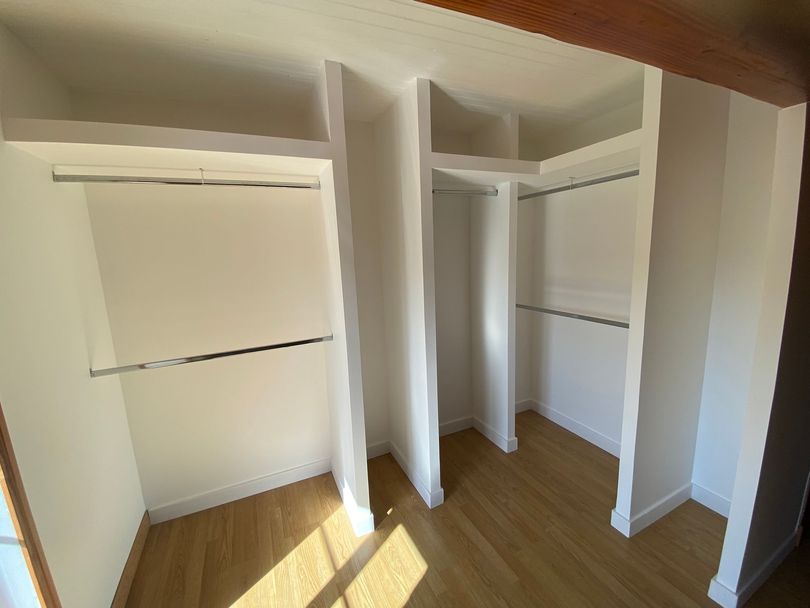 Un dressing vide avec des murs blancs, un sol en bois, des étagères et des tringles métalliques.
