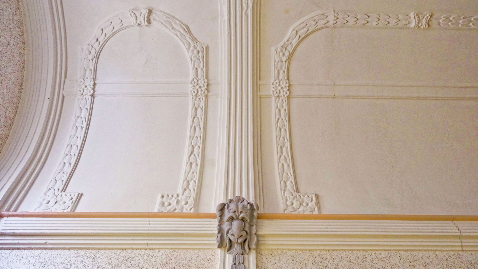 Eine reich verzierte, cremefarbene Wand mit dekorativen Stuckpaneelen und Goldverzierungen.
