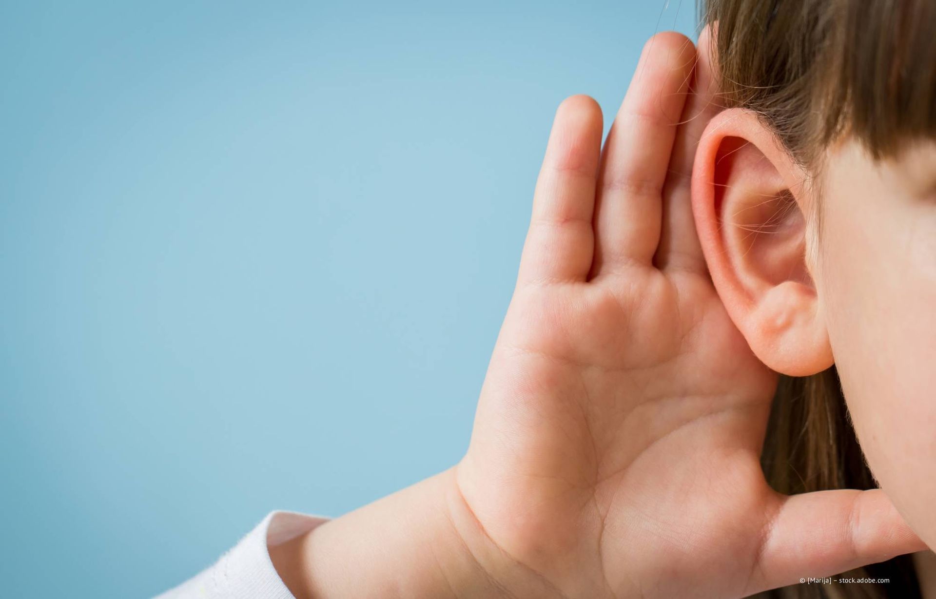 Nahaufnahme einer Person, die sich die Hand ans Ohr hält und aufmerksam zuhört, vor blauem Hintergrund.