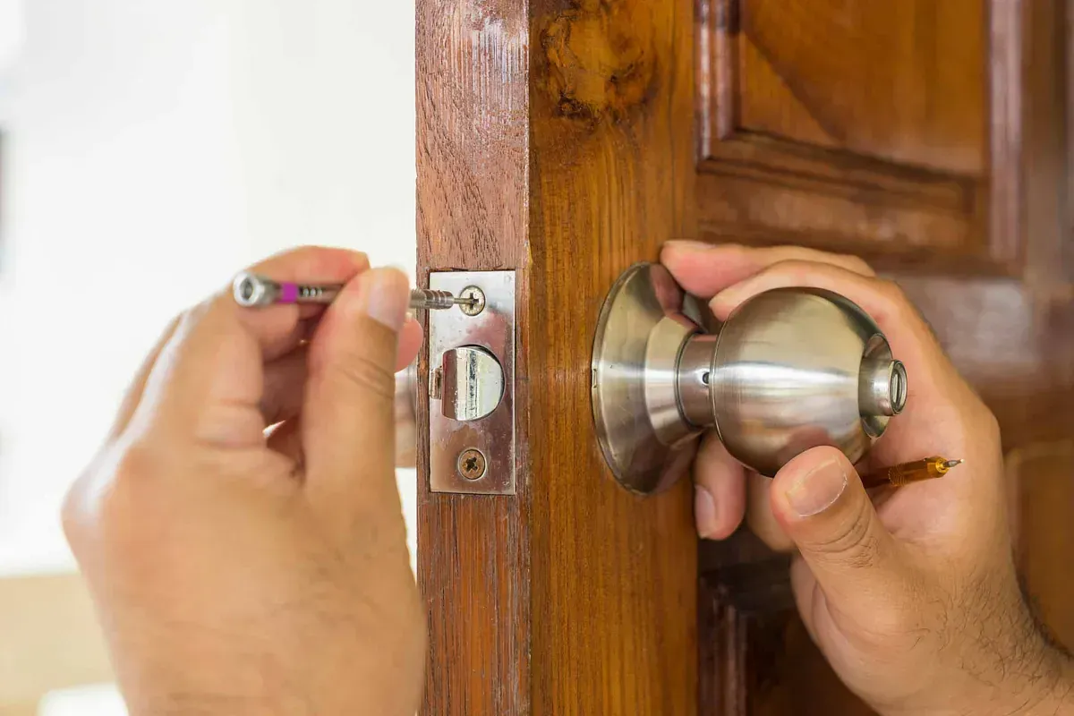 Una persona está arreglando una cerradura de puerta con un destornillador.