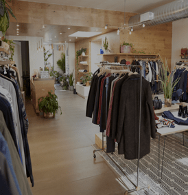 Intérieur d'un magasin de vêtements avec des portants, des murs en bois, des plantes et de la lumière naturelle.