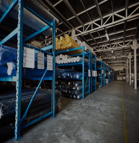 Des étagères métalliques bleues remplies de rouleaux de tissu se trouvent à l'intérieur d'un entrepôt.