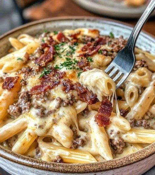 Plato de pasta con fideos penne, carne picada, salsa de queso y tocino desmenuzado. Un tenedor levanta un bocado.