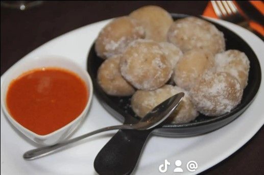 Papas pequeñas en un plato negro, servidas con salsa roja en un tazón blanco y dos cucharas, en un plato blanco.