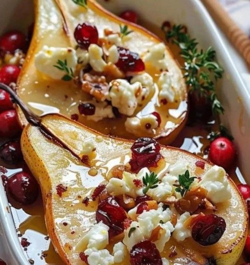 Mitades de pera asadas con arándanos, queso de cabra, nueces y miel en un plato blanco.