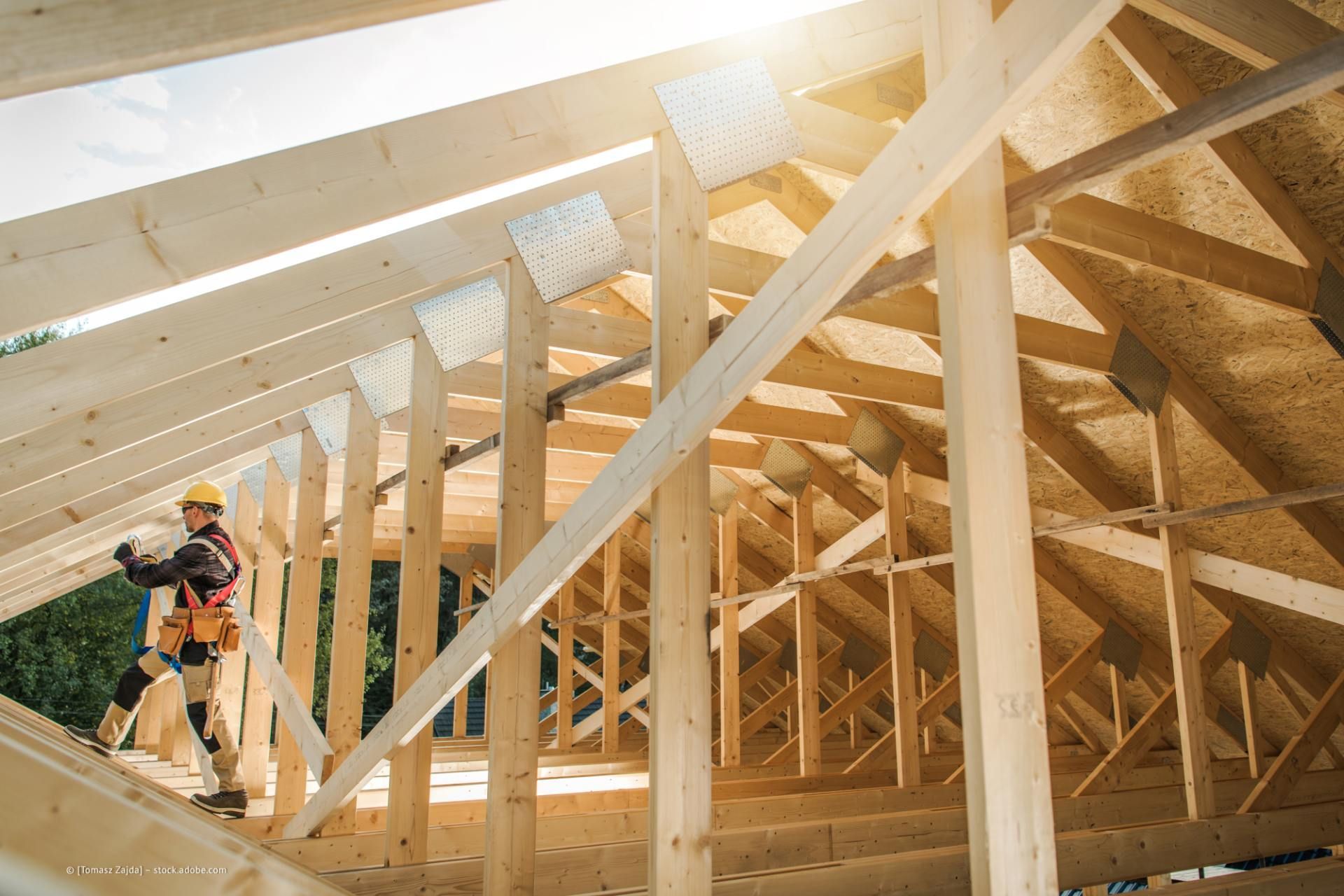Zimmermann arbeitet im hellen Sonnenlicht an einem hölzernen Dachstuhl.