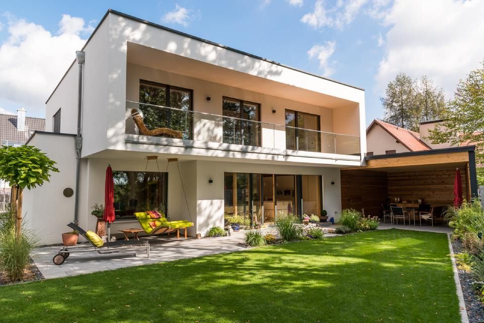 Modernes zweistöckiges Haus mit grünem Rasen, Gartenmöbeln und Balkon. Sonniger Tag.