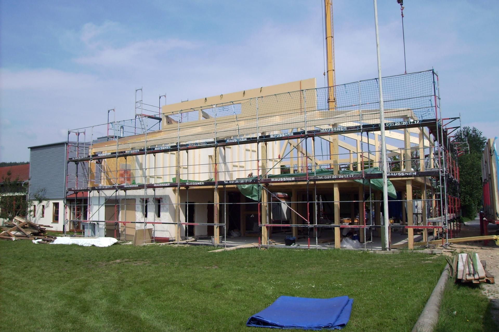 Gebäude im Bau mit Gerüst, Holzbalken und grünem Rasen.
